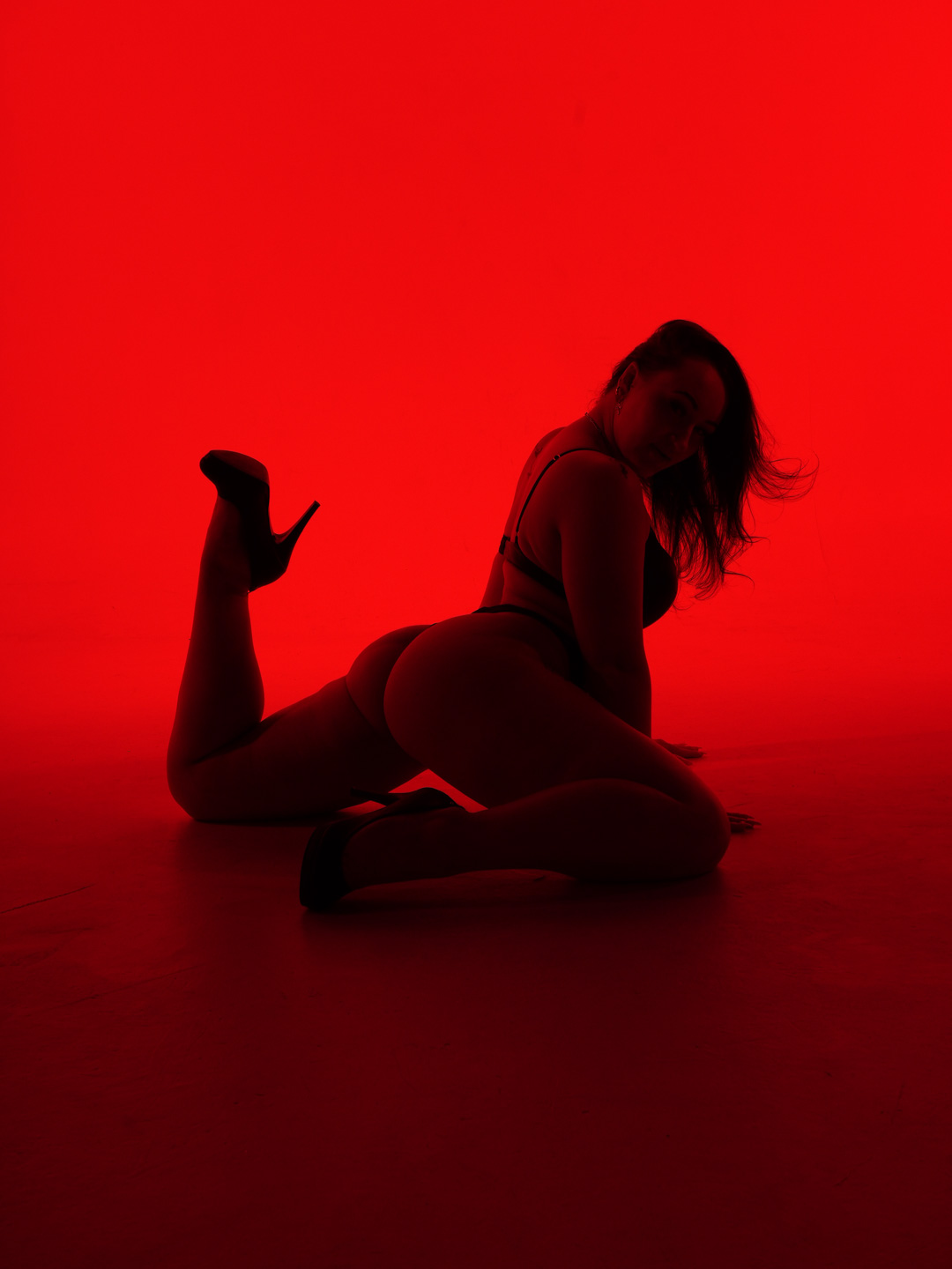 Paige Jade fully framed in a seated red-studio heels pose